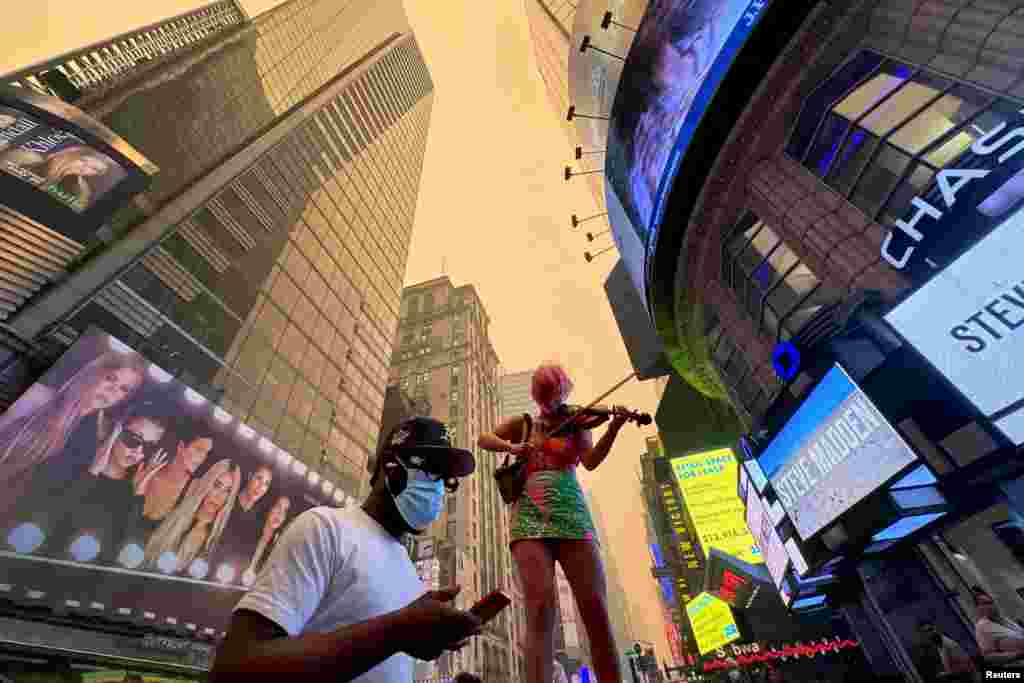 A performer plays the violin in Times Square as Manhattan is shrouded in haze and smoke which drifted south from wildfires in Canada, in New York City, June 7, 2023.