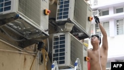 FILE - A handyman works on air conditioning units as summer temperatures soar in Hong Kong on Aug. 10, 2024. 