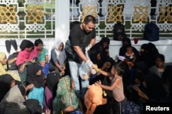Pengungsi Muslim Rohingya menerima makanan saat mereka beristirahat di trotoar di luar kantor pemerintah setelah mereka ditolak oleh penduduk setempat, setelah kedatangan mereka di Banda Aceh, 11 Desember 2023. (REUTERS/Riska Munawarah)