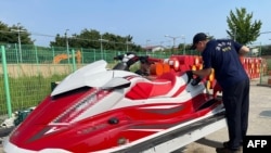 An undated handout photo made available by the South Korean coast guard shows two members in Incheon looking at the personal watercraft Kwon Pyong used to get to South Korea, crossing the Yellow Sea from the Chinese province of Shandong.