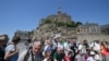 Turis berfoto bersama di depan Mont-Saint-Michel Prancis selama kunjungan dua hari Presiden Prancis di Normandia, di Le Mont-Saint-Michel, Prancis barat laut, 5 Juni 2023. (Jean -Francois MONIER / AFP)