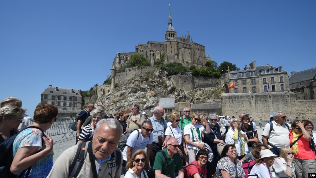 Turis berfoto bersama di depan Mont-Saint-Michel Prancis selama kunjungan dua hari Presiden Prancis di Normandia, di Le Mont-Saint-Michel, Prancis barat laut, 5 Juni 2023. (Jean -Francois MONIER / AFP)