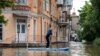 Seorang warga mendayung papan bantuan selama evakuasi dari daerah banjir, menyusul kerusakan yang terjadi di bendungan pembangkit listrik tenaga air Kakhovka, wilayah Kherson, Ukraina. (AFP)&nbsp;