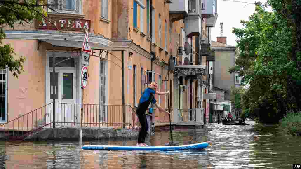 Seorang warga mendayung papan bantuan selama evakuasi dari daerah banjir, menyusul kerusakan yang terjadi di bendungan pembangkit listrik tenaga air Kakhovka, wilayah Kherson, Ukraina. (AFP)&nbsp;