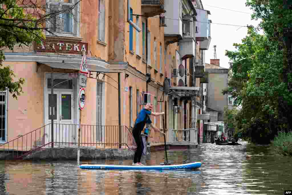 A local resident sails on a sup board during an evacuation from a flooded area in Kherson on June 8, 2023, following damages sustained at Kakhovka hydroelectric power plant dam.