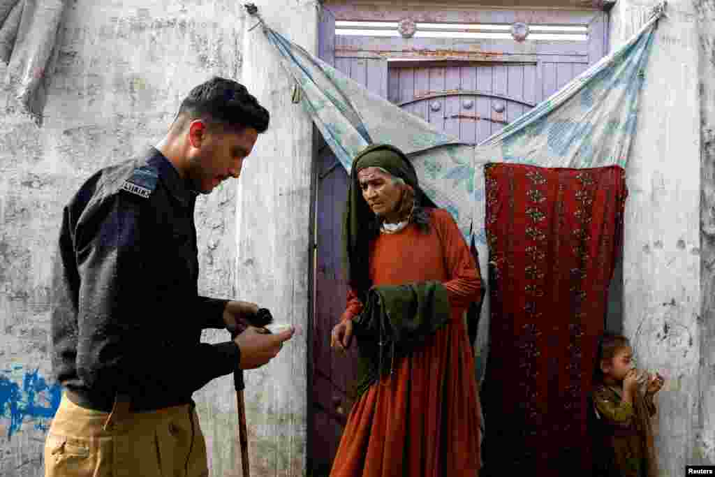 A police officer checks the registration card of Edema Bibi, 66, an Afghan citizen, outside her house in an Afghan Camp on the outskirts of Karachi, Pakistan,&nbsp;during a door-to-door search and verification drive for undocumented Afghan nationals, Nov. 21, 2023.