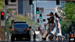 Olas de calor envuelven a dos mujeres que cruzan una calle de Phoenix, Arizona, el 17 de julio de 2023.