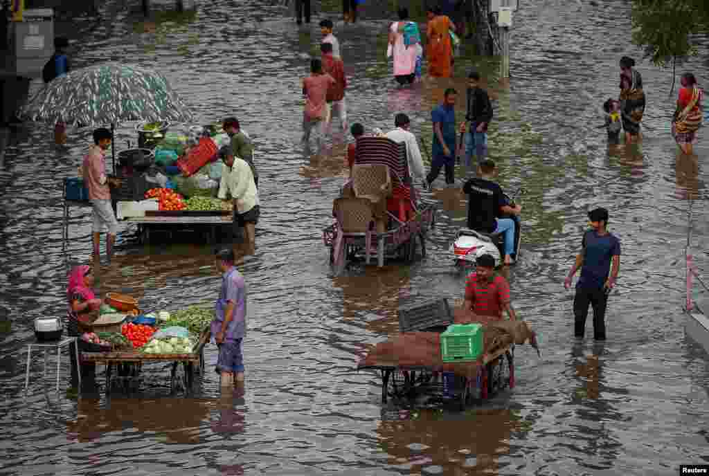 People buy vegetables from street vendors as others wade through a waterlogged road after heavy rains in Ahmedabad, India.