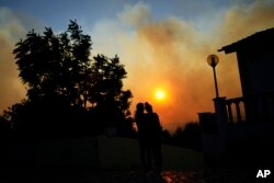 Two women watch a wildfire burning near houses in Alcabideche, outside Lisbon, Tuesday, July 25, 2023.