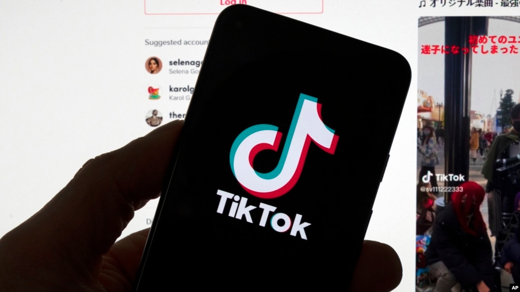 资料图片：在一台显示TikTok主屏幕的电脑前，人们看到手机上的 TikTok徽标。（波士顿，2023年3月 18日，波士顿）(photo:VOA)