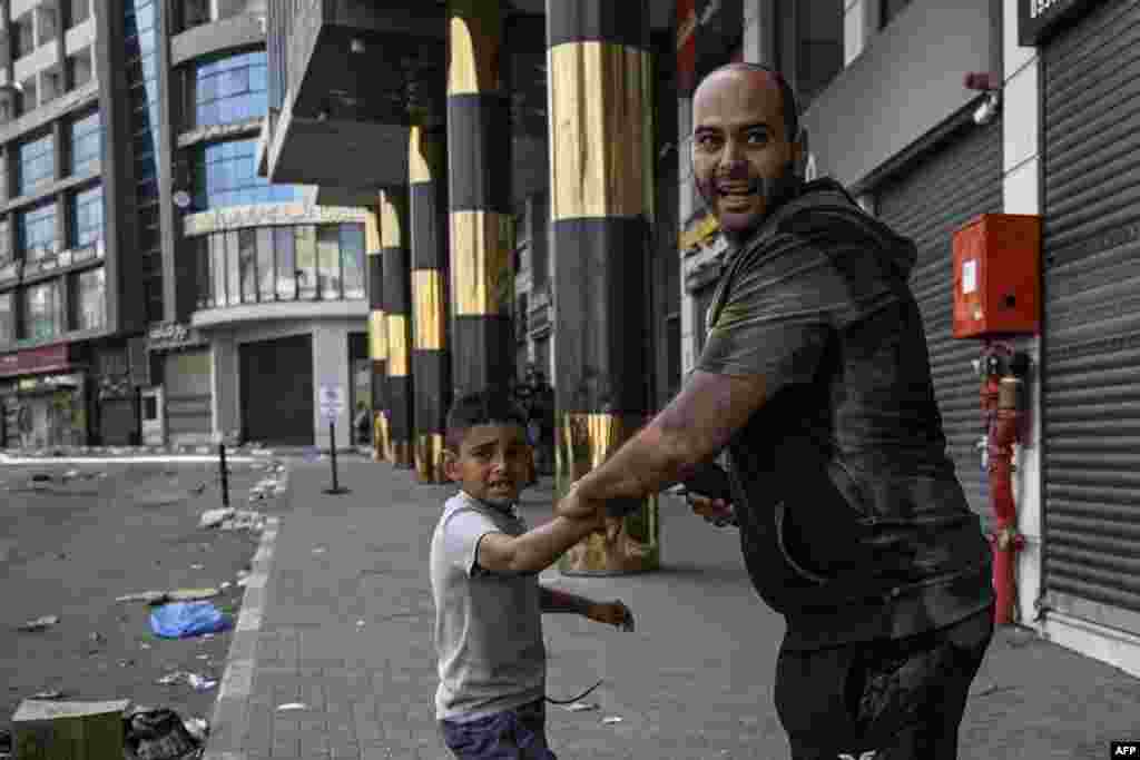 Seorang pria dan anak kecil bereaksi selama bentrokan antara tentara Israel dan orang-orang bersenjata Palestina di pusat Jenin di Tepi Barat yang diduduki Israel. Jalan-jalan sebagian besar sepi dan sebagian besar toko tutup di Tepi Barat, setelah ledakan keras dan bentrokan terdengar pada malam hari. (AFP)&nbsp;