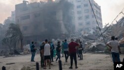 FILE - Journalists observe as Palestinians inspect the rubble of a building after it was struck by an Israeli airstrike, in Gaza City, Oct. 8, 2023.