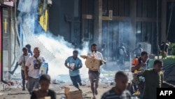 Orang-orang berlarian dengan barang-barang hasil jarahan di tengah kerusuhan di Port Moresby, ibu kota Papua Nugini, 10 Januari 2024. (Foto: Andrew Kutan/AFP)