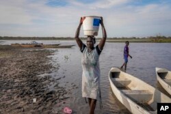 FILE -A woman carries water on her head from a swamp, with much of the area having no access to clean drinking water due to years of unprecedented flooding, in Canal-Pigi County, South Sudan, May 4, 2023.