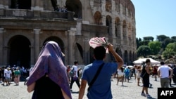 FILE - Tourists protect themselves from the sun as they walk near the Colosseum on July 11, 2024 in Rome. July temperatures reached the highest average on record worldwide, according to a U.S. environmental agency report. 