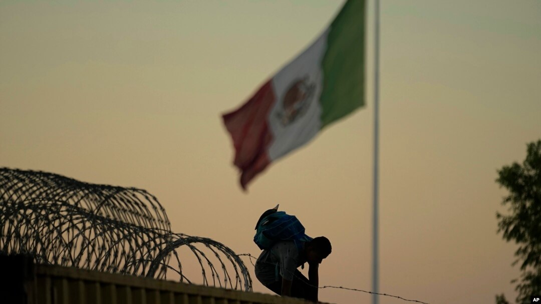Seorang migran yang melintasi Rio Grande dari Meksiko ke AS melewati penghalang kawat berduri dan mobil boks, Jumat, 22 September 2023, di Eagle Pass, Texas. (Foto: AP/Eric Gay)