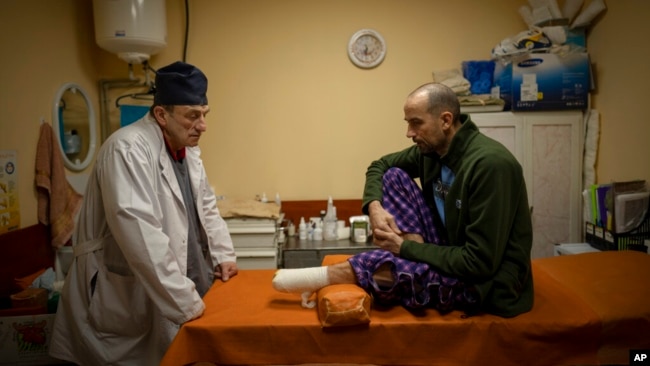 El médico ucraniano Yurii Kuznetsov habla con la víctima de las minas terrestres Oleksandr Kolisnyk en el hospital de Izium, Ucrania, el domingo 19 de febrero de 2023. (Foto AP/Vadim Ghirda, Archivo)