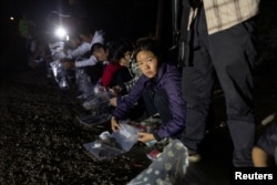 Seorang perempuan migran dari China menyimpan barang-barangnya di kantong pastik untuk diserahkan ke petugas Patroli Perbatasan AS setelah mereka menyeberangi Sungai Rio Grande dari Meksiko, di Fronton, Texas, 3 April 2023. (Foto: Staff/Reuters)