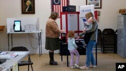 Lauren Miracle, right, holds her son Dawson, 1, as she helps her daughter Oaklynn, 3, fill out a child's practice ballot before voting herself at a polling location in the Washington Township House in Oregonia, Ohio, Nov. 7, 2023.