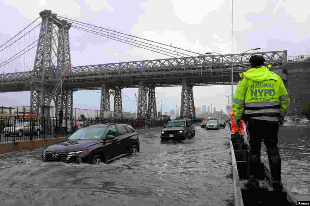 Um agente da polícia rodoviária de Nova Iorque observa os automobilistas a passarem por uma rua inundada após as fortes chuvas que provocaram inundações no meio do Atlântico e no Nordeste, na FDR Drive, perto da ponte de Williamsburg, em Nova Iorque, a 29 de setembro de 2023.