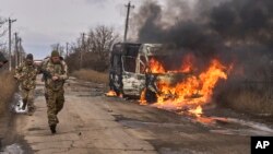 In this photo provided by Ukraine's military, Ukrainian soldiers pass by a bus burning after a Russian drone hit it near Bakhmut, Donetsk region, Ukraine, Nov. 23, 2023.
