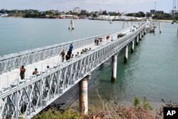 Masyarakat berjalan melintasi Jembatan Kaki Terapung Liwatoni yang baru diresmikan di Mombasa, Kenya, Jumat, 1 Januari 2021, yang dibangun oleh Otoritas Jalan Raya Nasional Kenya bekerja sama dengan China City Construction Company. (AP/ Gideon Mandu)