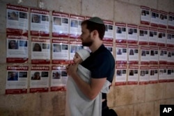 A man holds his baby as he looks at posters of the men, women and children held hostage by Hamas in the Gaza Strip, during a vigil marking 30 days since the October 7 Hamas attack that started the fighting, in Jerusalem, Nov. 5, 2023.