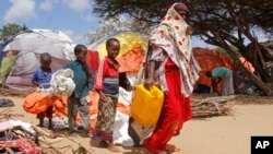 (FILE) A woman walks with her children, who fled amid drought, at a camp for the displaced people on the outskirts of Somalia.