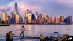 FILE — A man wades through a canal in Jersey City as the sun sets on the lower Manhattan skyline of New York City, May 31, 2022. (AP Photo/J. David Ake)