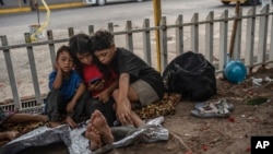 FILE - The Bolaños children, from left, Sebastian, Kamila and Miguel Angel, from Venezuela, watch videos on a mobile phone outside the bus terminal where they are living with their mother and one other sibling, in Villahermosa, Mexico, June 8, 2024. 