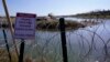 FILE - Migrants cross the Rio Grande into the U.S. from Mexico behind concertina wire and a sign warning that it's dangerous and illegal to cross, Jan. 3, 2024, in Eagle Pass, Texas.