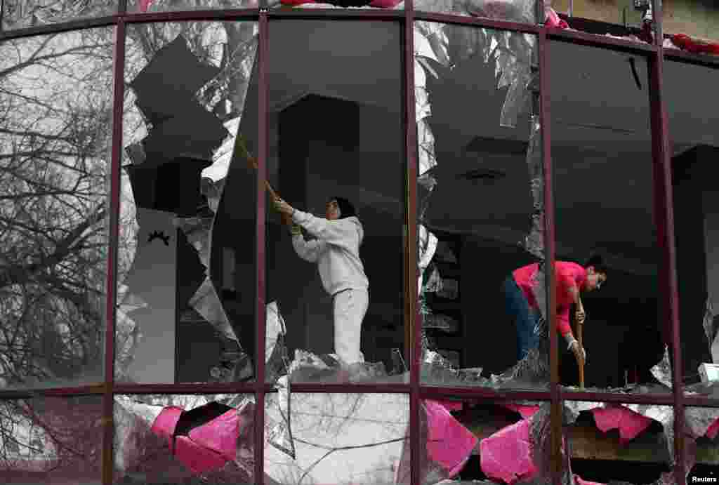 People remove shards of glass from broken windows of a building housing a beauty salon, following recent shelling in the course of Russia-Ukraine conflict in Donetsk, Russian-controlled Ukraine.