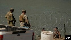 FILE - Guardsmen talk with migrants trying to cross the Rio Grande from Mexico into the U.S. near in Eagle Pass, Texas, July 11, 2023.