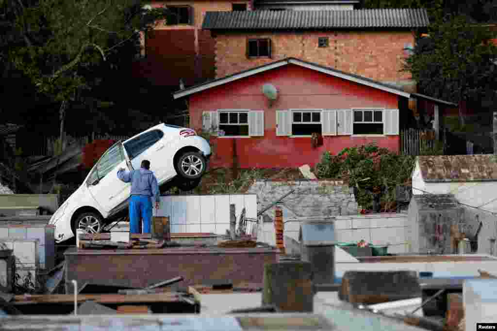 A man checks a car which lays on top of graves at the Pedro Freiberger cemetery as a result of flooding due to heavy rains following an extratropical cyclone, in Caraa, Rio Grande do Sul state, Brazil.