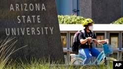 FILE - A cyclist crosses an intersection on the campus of Arizona State University on Sept. 1, 2020, in Tempe, Ariz.