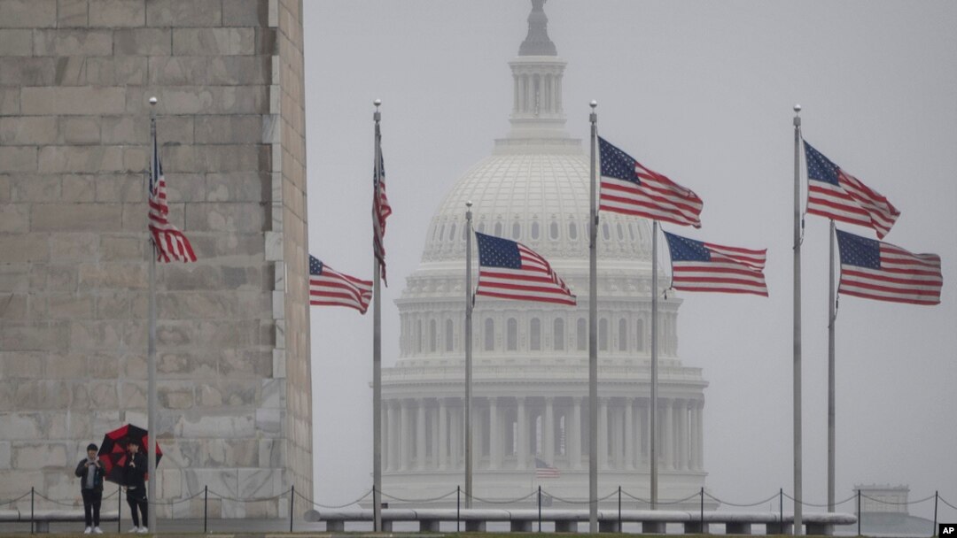 Visitors stand at the base of the Washington Monument as the dome of the Capitol is seen in the distance, in Washington, March 5, 2024.