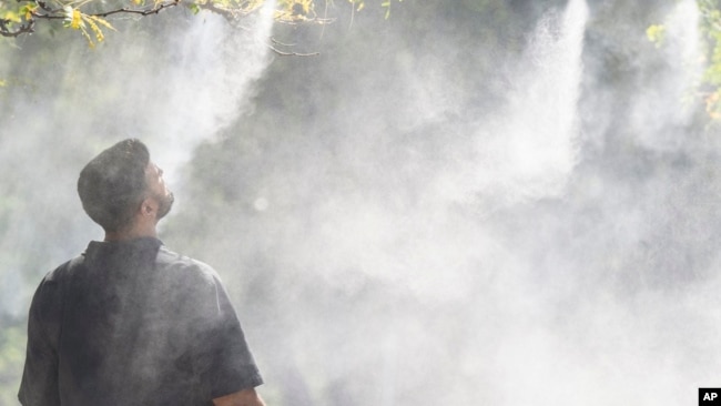 FILE - A man stands under a mister to cool off from the heat in Montreal, Sept. 6, 2023.