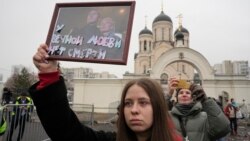 Seorang perempuan memegang potret Alexey Navalny dan istrinya, Yulia, di luar gereja tempat pemakamannya berlangsung, di Moskow, Rusia, 1 Maret 024. (Foto: AP Photo)