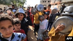 Anak-anak pengungsi Palestina antre sambil membawa panci dan wajan saat para sukarelawan membagikan makanan hangat di Khan Yunis di Jalur Gaza selatan, 23 November 202. (Mahmud HAMS/AFP)
