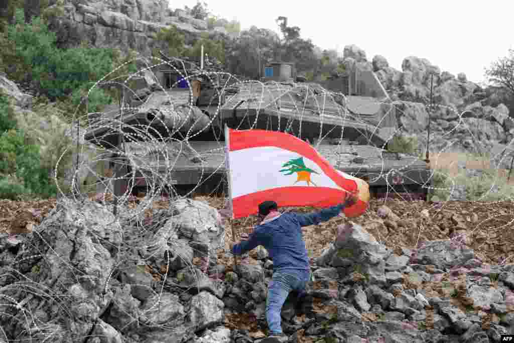 A Lebanese protester plants the national flag across the fence from an Israeli tank during an anti-Israeli demonstration near the &quot;blue line&quot; area, a demarcation line drawn by the U.N. to mark Israel&#39;s withdrawal from southern Lebanon in 2000, near the Lebanese southern village of Kfar Shuba.