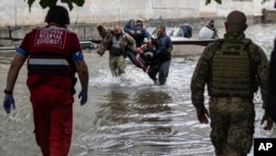 Petugas evakuasi bergegas membantu warga yang terluka akibat serangan yang diduga dilancarkan pasukan Rusia dalam proses evakuasi warga dari banjir di wilayah Kherson, Ukraina, pada 11 Juni 2023. (Foto: AP)