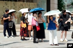 FILE - Pedestrians hold parasols to shield themselves from the sun in Tokyo, July 8, 2024.