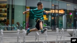 一个男孩在北京街头的喷水池玩水。（2023年7月1日）