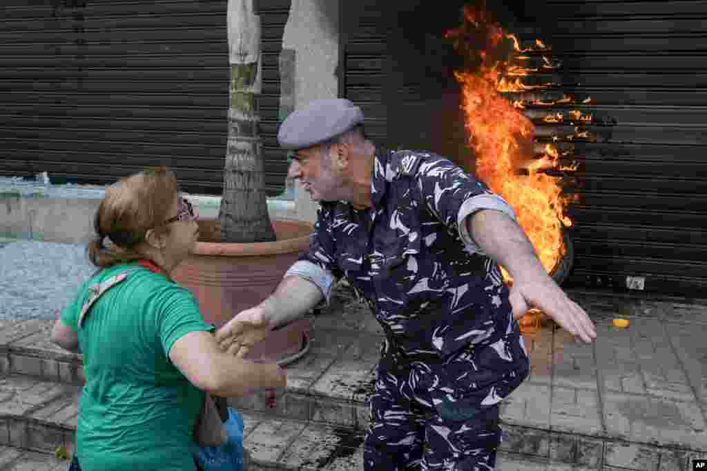 A police officer speaks with a protesting depositor as they stand in front of burning tires set on fire in front of a branch of Emirates Lebanese Bank in Dawra, a suburb north-east of Beirut, Lebanon.&nbsp;Depositors demand their trapped savings deposits as they struggle from an economic crisis.