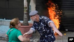 A police officer speaks with a protesting depositor as they stand in front of burning tires set on fire in front of a branch of Emirates Lebanese Bank in Dawra, a suburb north-east of Beirut, Lebanon.&nbsp;Depositors demand their trapped savings deposits as they struggle from an economic crisis.