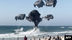 This image grab from an AFPTV video shows Palestinians running toward parachutes attached to food parcels, air-dropped from US aircrafts on a beach in the Gaza Strip on March 2, 2024.