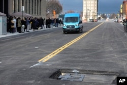 An electric van drives near a visible in-road wireless charging coil to be installed in a street in Detroit, Wednesday, Nov. 29, 2023. (AP Photo/Paul Sancya)