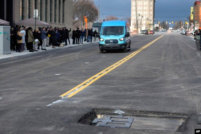 An electric van drives near a visible in-road wireless charging coil to be installed in a street in Detroit, Wednesday, Nov. 29, 2023. (AP Photo/Paul Sancya)