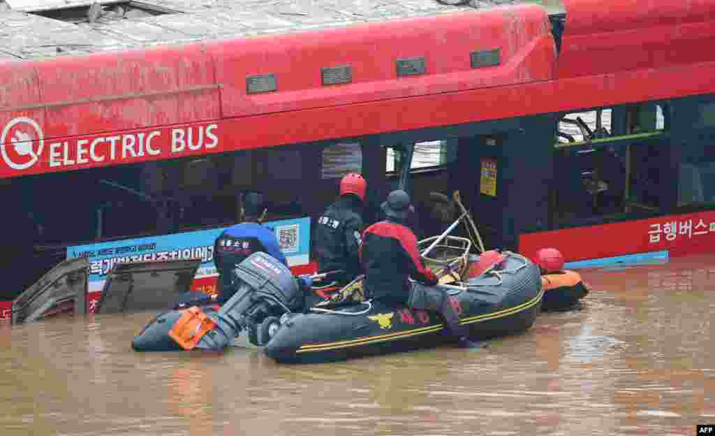 South Korean rescue workers search for missing persons near a bus along a deluged road leading to an underground tunnel where some 15 cars were trapped in flood waters after heavy rains in Cheongju.