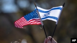 Seorang peserta memegang miniatur bendera AS dan Israel pada Selasa, 14 November 2023, di Washington. (Foto: AP)